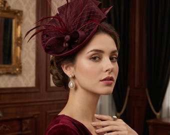 Puede incluir: Un tocado de color burdeos profundo con una base estructurada, red delicada y plumas decorativas. La pieza está adornada con pequeños detalles circulares a juego y se lleva con un top de terciopelo burdeos y pendientes de perlas a juego.