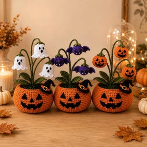 Può includere: Tre piante in vaso all'uncinetto a tema Halloween. Ogni vaso è arancione con una faccia di zucca nera e un piccolo cappello da strega. Le piante presentano fantasmi bianchi, pipistrelli viola e zucche arancioni su steli verdi con foglie.
