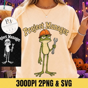 May include: A light yellow t-shirt featuring a graphic of a green frog wearing an orange hard hat and holding a silver wrench. The text "Project Manager" is printed in a curved, bold, dark font above the frog illustration.