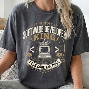 Könnte beinhalten: Ein anthrazitfarbenes Kurzarm-T-Shirt mit einem Grafikdruck und dem Text I'M THE SOFTWARE DEVELOPER KING I CAN CODE ANYTHING. Das Design zeigt einen Computermonitor mit einer Krone, Leiterplattenmuster und Programmiersymbole.