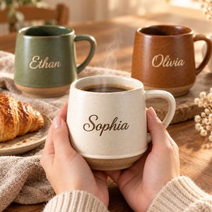 Puede incluir: Tres tazas de cerámica con acabado moteado y nombres grabados en letra cursiva. Una taza es color crema con el nombre Sophia, otra es verde salvia con Ethan y otra es marrón terracota con Olivia. Cada taza tiene un asa lateral.