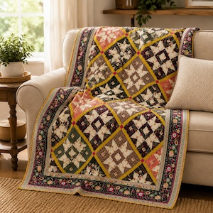 May include: A quilted throw blanket featuring a repeating star pattern in shades of mustard yellow, deep burgundy, forest green, and cream. The quilt is bordered by a dark fabric with a colorful floral print and finished with a thin yellow binding.