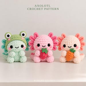 Könnte beinhalten: Drei gehäkelte Axolotl-Stofftiere mit schwarzen Augen und rosa Wangen. Das linke trägt eine grüne Froschkapuze. Das mittlere hält eine rote Erdbeere. Das rechte hält eine orangefarbene Karotte. Text: AXOLOTL CROCHET PATTERN und RURARU STUDIO.