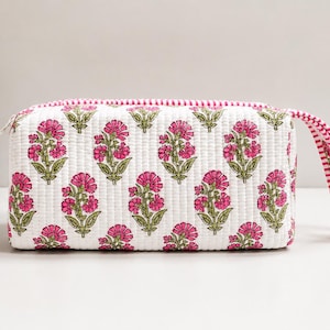 Könnte beinhalten: Eine rechteckige, gesteppte Tasche mit weißem Grund und einem sich wiederholenden Muster aus rosa Blumen und grünen Stielen. Die Tasche verfügt über einen Reißverschluss und eine passende, gestreifte Handschlaufe in Rosa und Weiß.