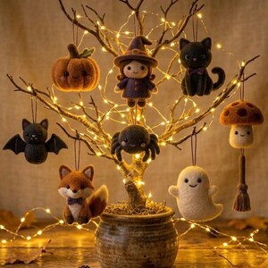 Könnte beinhalten: Ein dekorativer Baum mit warmen Lichterketten zeigt Filzanhänger, darunter ein Kürbis, eine Hexe, eine schwarze Katze, eine Fledermaus, eine Spinne, ein Fuchs, ein Geist und ein Pilz mit Quaste. Jeder Anhänger hängt an einem dünnen Faden.