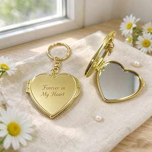 May include: A gold-toned heart-shaped compact mirror keychain with a metal ring. One side is closed and engraved with the text Forever in My Heart, while the other side is open to reveal a reflective mirror surface.