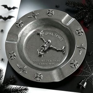 May include: A circular silver-toned metal ashtray featuring a central skeleton figure and the text "DARK SPIRIT" and "HALLOWEEN & DARK CHRISTMAS". The rim is decorated with alternating cross and floral-shaped emblems in a metallic finish.