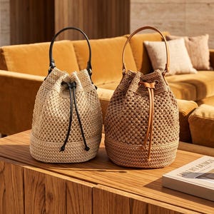 Könnte beinhalten: Zwei Beuteltaschen aus geflochtenem Strohmaterial. Die linke Tasche ist hellbeige mit einem schwarzen Griff und Kordelzug. Die rechte Tasche ist in einem dunkleren Braunton gehalten und hat einen passenden Griff und Kordelzug. Beide haben einen festen Boden.