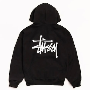 Op de afbeelding: Een zwarte hoodie met lange mouwen en een wit Stüssy-logo op de achterkant. Het kledingstuk is voorzien van een capuchon, geribbelde boorden aan de mouwen en een geribbelde zoom aan de onderkant, weergegeven vanuit een achteraanzicht.