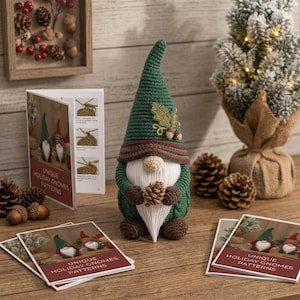 May include: A crocheted gnome figurine with a tall green hat, a white beard, and brown hands holding a small pinecone. The gnome features an embroidered oak leaf and acorn detail on the hat. Several printed pattern booklets titled Unique Holiday Gnomes Patterns are displayed alongside the gnome.