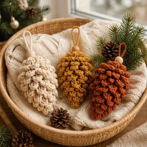 Op de afbeelding: Drie handgemaakte macramé dennenappelhangers in crème, mosterdgeel en roestoranje. Elke hanger heeft een getextureerd knoopontwerp, een houten kraal aan de bovenkant en een bijpassende koordlus om de decoratie mee op te hangen.