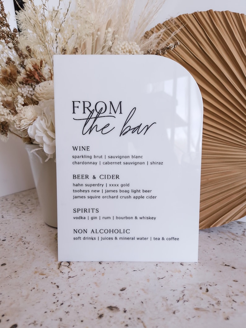 May include: A white arched acrylic sign with black text reading FROM the bar, listing categories for WINE, BEER & CIDER, SPIRITS, and NON ALCOHOLIC with various drink options including sparkling brut, sauvignon blanc, and others.