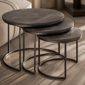 Peut inclure: Un ensemble de trois tables gigognes dotées de plateaux circulaires en pierre gris foncé avec un veinage subtil. Chaque table est soutenue par une fine structure en métal noir avec une base incurvée, permettant aux tables de s'emboîter.