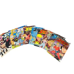 May include: A collection of nine Zot! comic books by Eclipse Comics arranged in a fan shape. Each cover features colorful illustrations of characters, including a blonde hero in a red suit, with bold text titles and various action scenes.