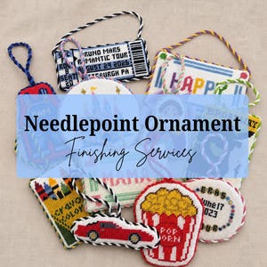 May include: A collection of various needlepoint ornaments featuring diverse designs including a concert ticket, a popcorn bucket, a red car, and colorful text. Each ornament is finished with a twisted cord hanger in matching or contrasting colors.