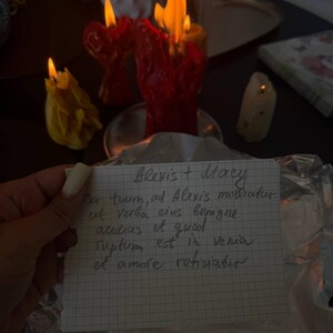 A hand holding a handwritten note with a candlelit candle in the background.