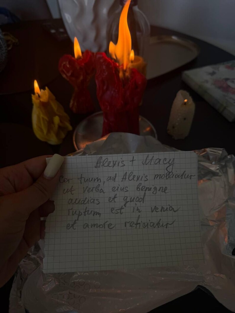 A hand holding a handwritten note with a candlelit candle in the background.
