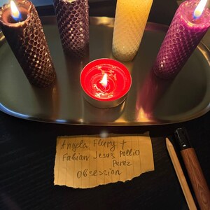 a tray with four candles of different colors - purple, yellow, and red - along with a red candle and a handwritten note.