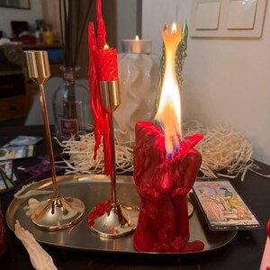 a table with a lit red candle, a partially melted candle, and a tarot card.