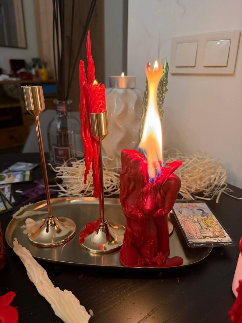 a table with a lit red candle, a partially melted candle, and a tarot card.