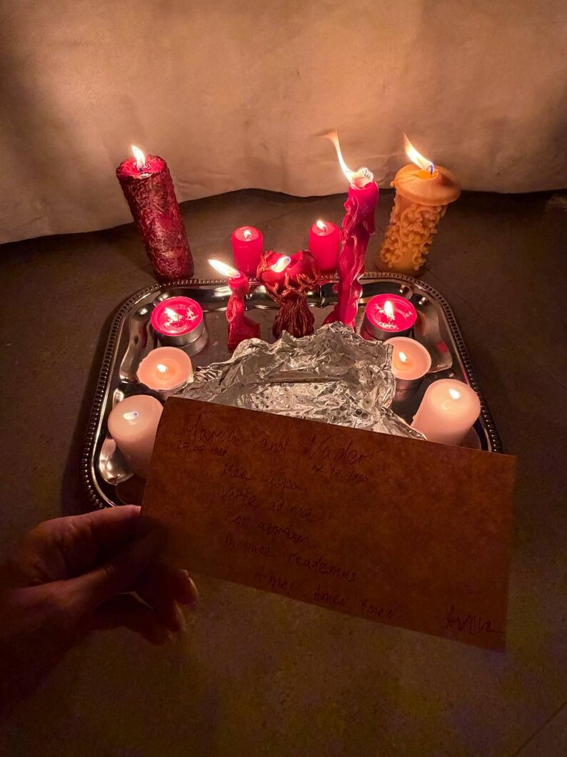 A hand holds a handwritten note in front of a tray with lit candles, creating a warm and intimate atmosphere.