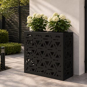 Puede incluir: Una jardinera rectangular de metal negro con un patrón geométrico recortado de triángulos y barras horizontales. Dos plantas de hortensias blancas en macetas con hojas verdes están colocadas en la parte superior de la estructura sobre un patio.