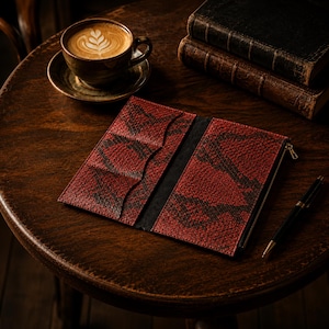May include: A long, rectangular wallet featuring a red and black snakeskin-textured pattern. The interior is open, revealing multiple card slots on the left side and a zippered compartment on the right side, with black lining throughout the interior.