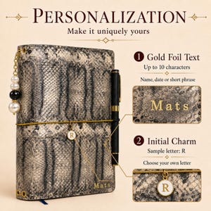 May include: A notebook with a grey and black snakeskin pattern cover, featuring a gold elastic band, a black pen, and a dangling charm with the letter R. The cover displays the gold foil text Mats, with additional text explaining personalisation options.