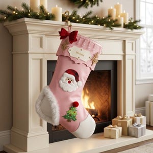 May include: A light pink Christmas stocking featuring a white faux fur cuff and toe. The stocking is decorated with a red bow, a Santa Claus applique, and a green Christmas tree with a red pom-pom. A white name tag with the name Melissa is attached.