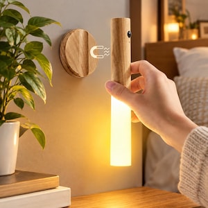 May include: A cylindrical light fixture with a light wood grain finish and a frosted white lower section that emits a warm glow. The light features a small black sensor and attaches to a circular wooden wall mount via a magnetic connection.
