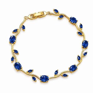 May include: A gold-toned bracelet featuring a vine-like structure with alternating blue oval-shaped stones and small leaf-shaped accents. The piece includes a secure metal clasp mechanism and a continuous, flexible design that wraps around the wrist.