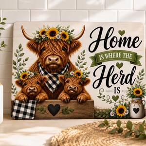 Pode incluir: Uma placa retangular de madeira com uma vaca Highland castanha e dois vitelos com coroas de girassóis e uma bandana axadrezada preta e branca. O texto diz Home IS WHERE THE Herd IS, decorado com folhas verdes, corações e girassóis.