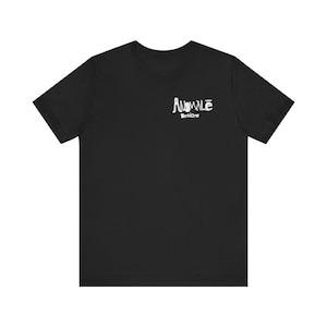 以下が含まれることがあります： 左胸上部に白いグラフィックが施された黒の半袖Tシャツ。グラフィックには、手書き風のスタイリッシュなフォントで「ANOMALĒ DESIGNS」という文字が描かれており、Eの文字の上には水平線が引かれています。
