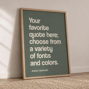 May include: A rectangular wall art print in a light wood frame featuring a sage green background with white text that reads: Your favourite quote here; choose from a variety of fonts and colours. - Author (optional). The print is displayed vertically.