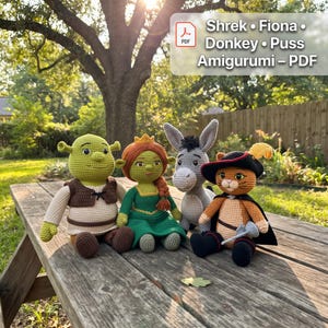 Op de afbeelding: Vier gehaakte amigurumi-poppen die Shrek, Fiona, Ezel en de Gelaarsde Kat voorstellen. De tekst Shrek Fiona Donkey Puss Amigurumi PDF is zichtbaar in de hoek. De poppen hebben gedetailleerd haakwerk, inclusief kleding, hoeden en capes.