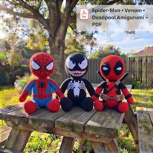 May include: Three crocheted amigurumi dolls featuring Spider-Man, Venom, and Deadpool. Spider-Man is red and blue with a black spider emblem. Venom is black with a white spider emblem and sharp teeth. Deadpool is red and black with utility belts.