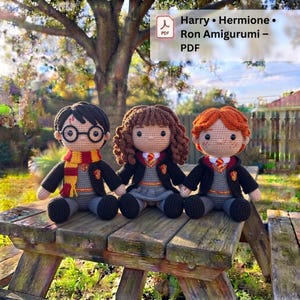 May include: Three amigurumi dolls representing characters with brown, curly brown, and orange yarn hair. They wear black robes over grey sweaters with yellow and red accents, including ties and scarves. The text reads Harry • Hermione • Ron Amigurumi – PDF.