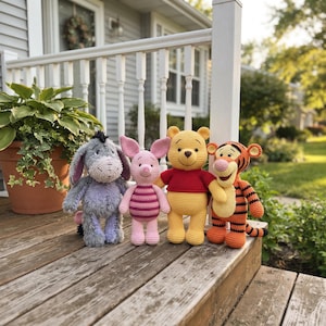 May include: Four crocheted stuffed animals standing in a row. From left to right: a grey donkey with long ears, a small pink pig with dark pink stripes, a yellow bear wearing a red shirt, and an orange tiger with black stripes and a long tail.