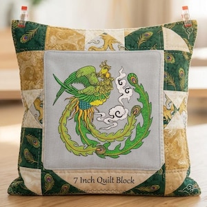 May include: A square quilt block featuring a central light gray panel with an embroidered green and yellow phoenix design. The border consists of alternating green and gold fabric squares with peacock feather patterns. Text reads 7 Inch Quilt Block.