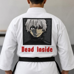 Peut inclure: Un kimono d'arts martiaux blanc avec un grand écusson carré brodé dans le dos. L'écusson représente un personnage d'anime stylisé aux cheveux blancs avec un œil rouge. Sous l'écusson, le texte Dead Inside est brodé en lettres rouges.