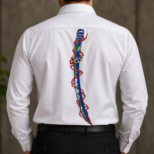 Può includere: Una camicia bianca a maniche lunghe con colletto abbottonato, caratterizzata da un grande ricamo dettagliato sul retro. Il disegno raffigura una spada curva blu e verde avvolta da un filo rosso vivace, centrata verticalmente sulla schiena.