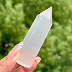 Può includere: Una torre di cristallo bianca e traslucida a sei lati con una punta acuminata. L'oggetto presenta una superficie liscia e lucida e una base cilindrica che si restringe in una forma a piramide esagonale all'apice, con un aspetto vitreo.