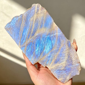 Può includere: Una lastra piatta e rettangolare di minerale labradorite caratterizzata da un vibrante riflesso blu iridescente sulla superficie. La pietra presenta un aspetto naturale e strutturato con venature chiare incrociate e una finitura lucida.