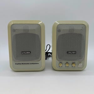 May include: A pair of beige Koss amplified multimedia loudspeakers with rectangular frames and silver mesh grilles. The left speaker features the text Amplified Multimedia Loudspeakers, while the right speaker includes three control knobs and a power switch.