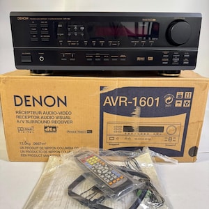 May include: A black Denon AVR-1601 A/V surround receiver sits atop its original cardboard box. The box features the model name, technical specifications, and logos. Included are a remote control and an antenna in plastic packaging.