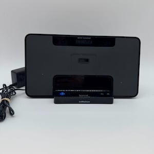 May include: A black Altec Lansing speaker dock with a rectangular mesh grille, a digital display showing FM 107.1, and a central docking port. The device features a power button with a blue light and the word inMotion printed on the base.