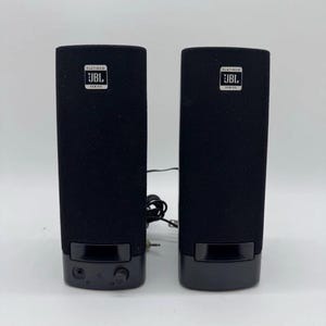 May include: A pair of black JBL Platinum Series computer speakers with a fabric-covered front grille. The left speaker features a volume control knob and a headphone jack at the base. Both units display a white JBL logo badge near the top.