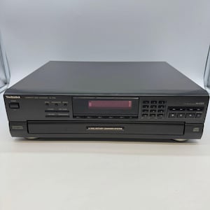 Puede incluir: Un reproductor de discos compactos Technics SL-PD6 negro con un sistema de cambiador giratorio de 5 discos. El panel frontal incluye un botón de encendido, pantalla digital, teclado numérico, botones de control de reproducción y tecnología MASH.