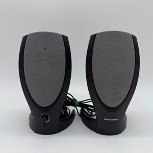 Può includere: Una coppia di altoparlanti per computer Harman Kardon neri con griglie in rete grigia. L'altoparlante sinistro presenta una manopola circolare per il volume alla base, mentre quello destro mostra il logo Harman Kardon in bianco sul davanti.