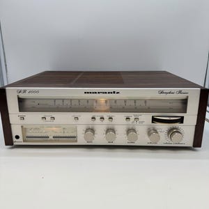 May include: A Marantz SR 4000 stereophonic receiver with a silver front panel and a dark wood grain cabinet. The unit features a horizontal radio tuning display, multiple control knobs for bass, mid, treble, selector, and volume, and a power meter.